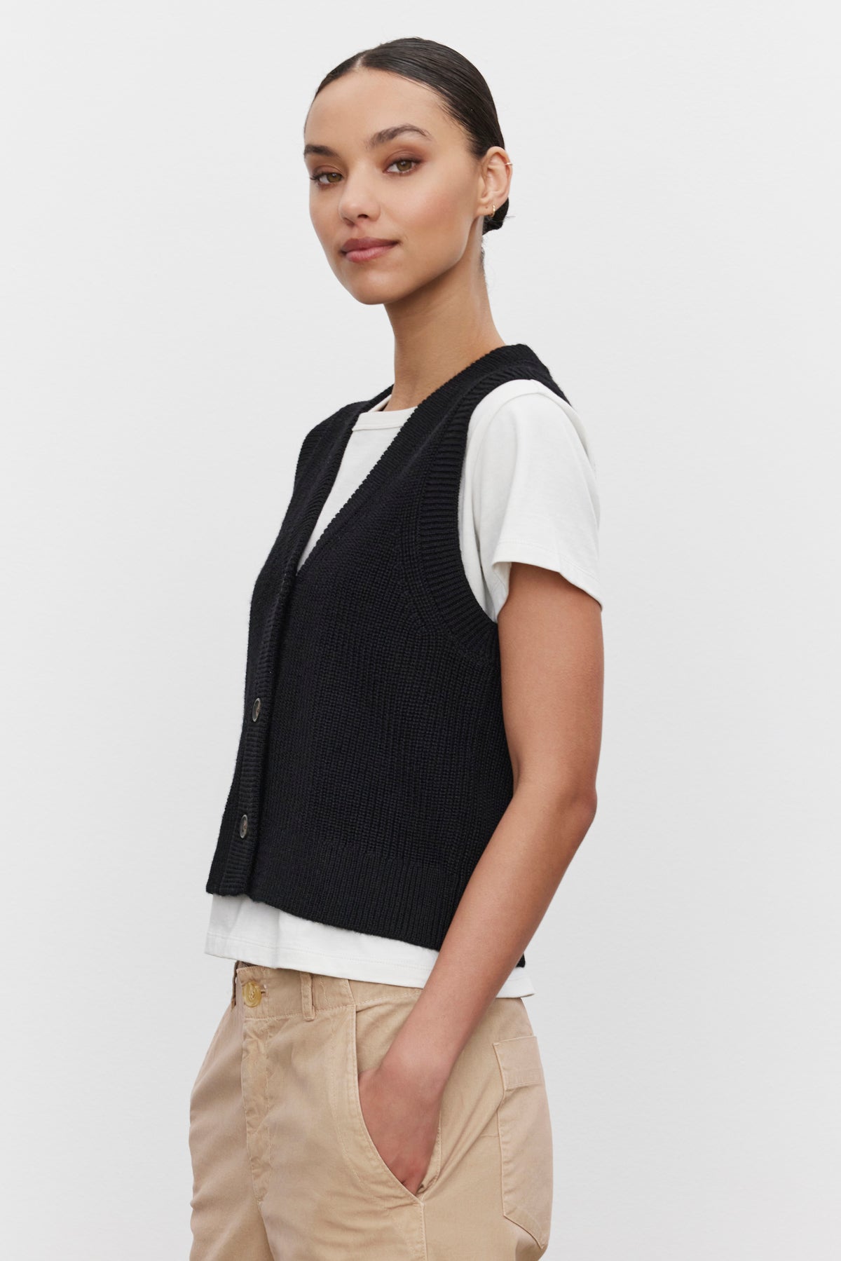 A person wearing the LU SWEATER VEST by Velvet by Graham & Spencer over a white t-shirt and beige pants, standing against a plain white background.-37676225233089