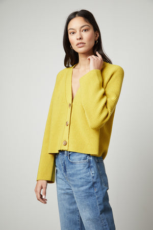 The model is wearing the Marilyn Button Front Cardigan in sunflower yellow by Velvet by Graham & Spencer and jeans.
