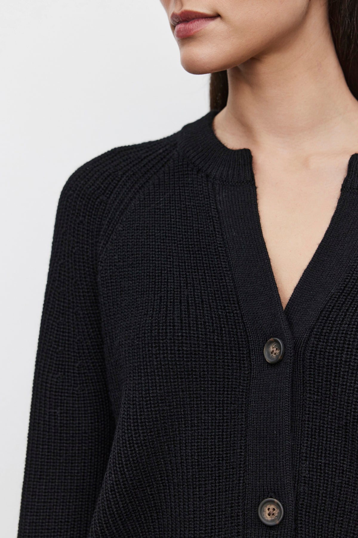   Close-up of a person wearing the SHAYLA CARDIGAN, a cozy black buttoned piece with a textured knit pattern from Velvet by Graham & Spencer. Crafted from a wool blend, the focus is on the garment, highlighting its rich fabric alongside part of the person's face. 