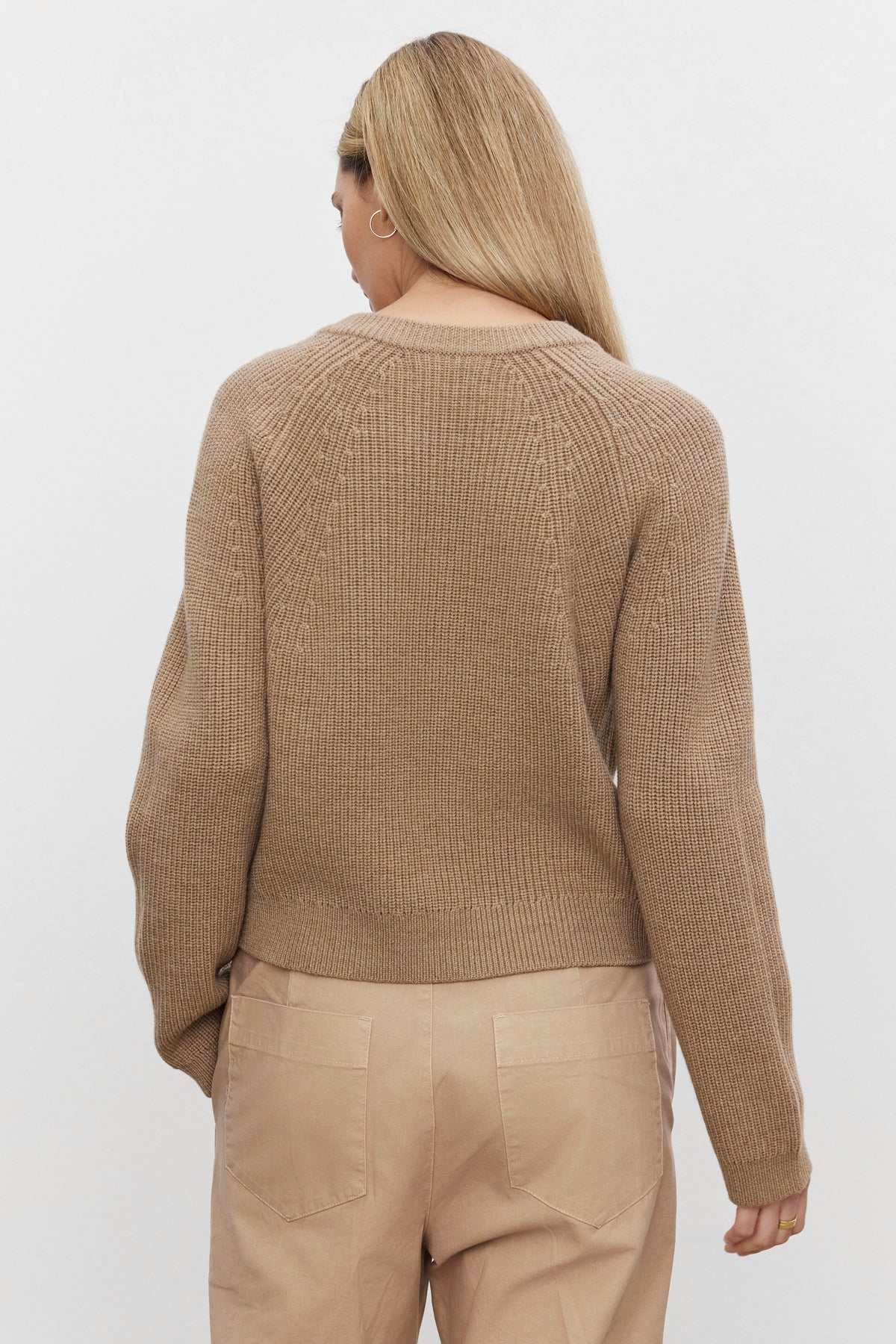   A person with long blonde hair is shown from behind, wearing the SHAYLA CARDIGAN by Velvet by Graham & Spencer and relaxed-fit beige pants against a plain white background. 