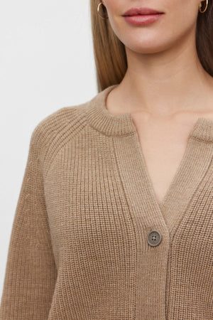 Close-up of a person wearing the SHAYLA CARDIGAN by Velvet by Graham & Spencer, featuring a light brown hue and a single button fastened in the middle. The relaxed fit elegantly highlights the collarbone, neck, and part of the face.