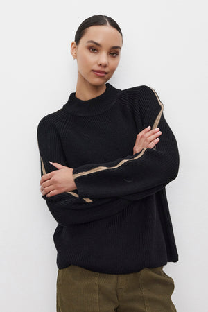 A person wearing the TEAGAN SWEATER by Velvet by Graham & Spencer, a black wool blend piece featuring light stripes on the sleeves, stands against a white background with their arms crossed.