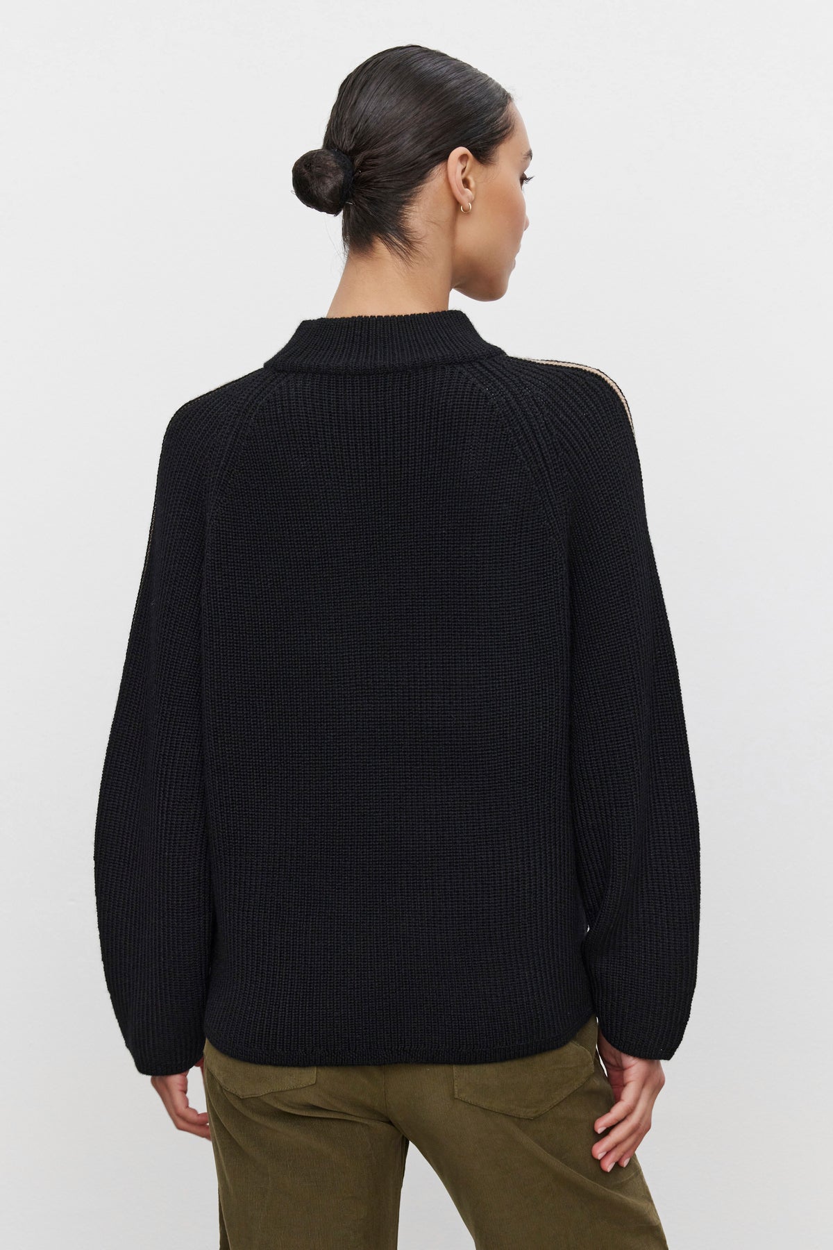   A woman with her hair in a bun is wearing the TEAGAN SWEATER from Velvet by Graham & Spencer, a cozy and comfortable black long-sleeve wool blend with a mock neck design, paired with dark olive pants. She is shown from the back against a plain white background. 