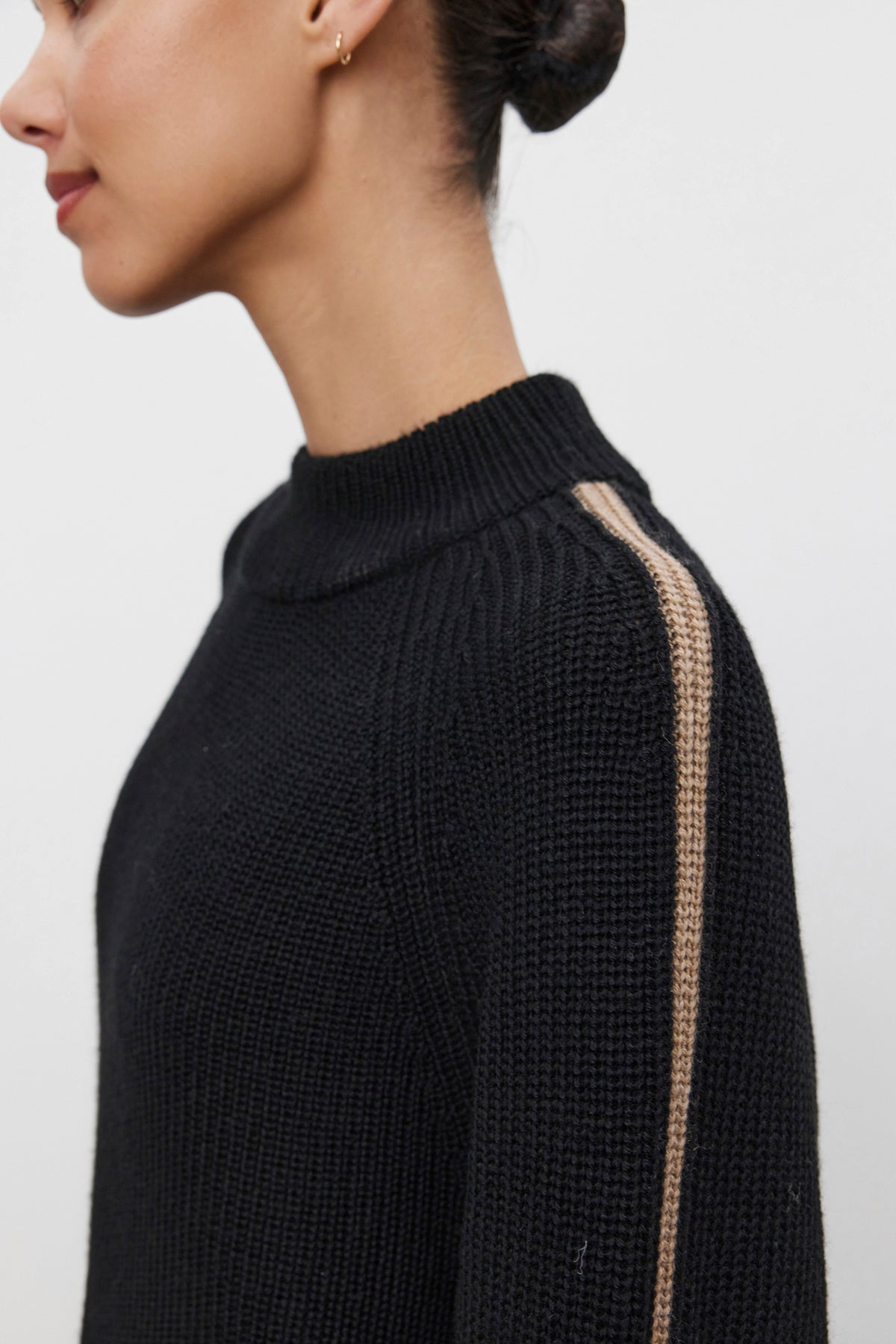   A person wearing the TEAGAN SWEATER from Velvet by Graham & Spencer, a black knit wool blend sweater featuring a single beige stripe on the sleeve, shown from the side. 