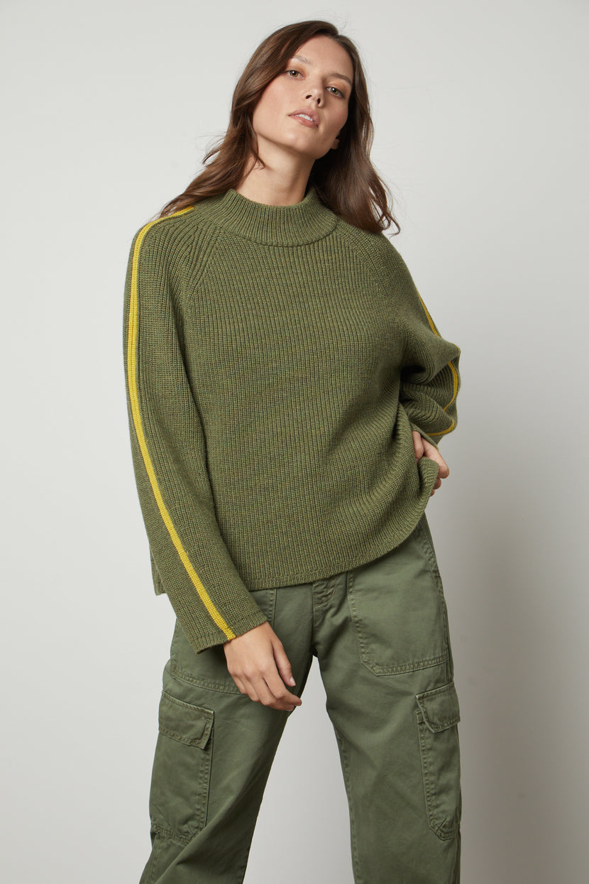 The model is wearing a TEAGAN MOCK NECK SWEATER by Velvet by Graham & Spencer and yellow cargo pants.