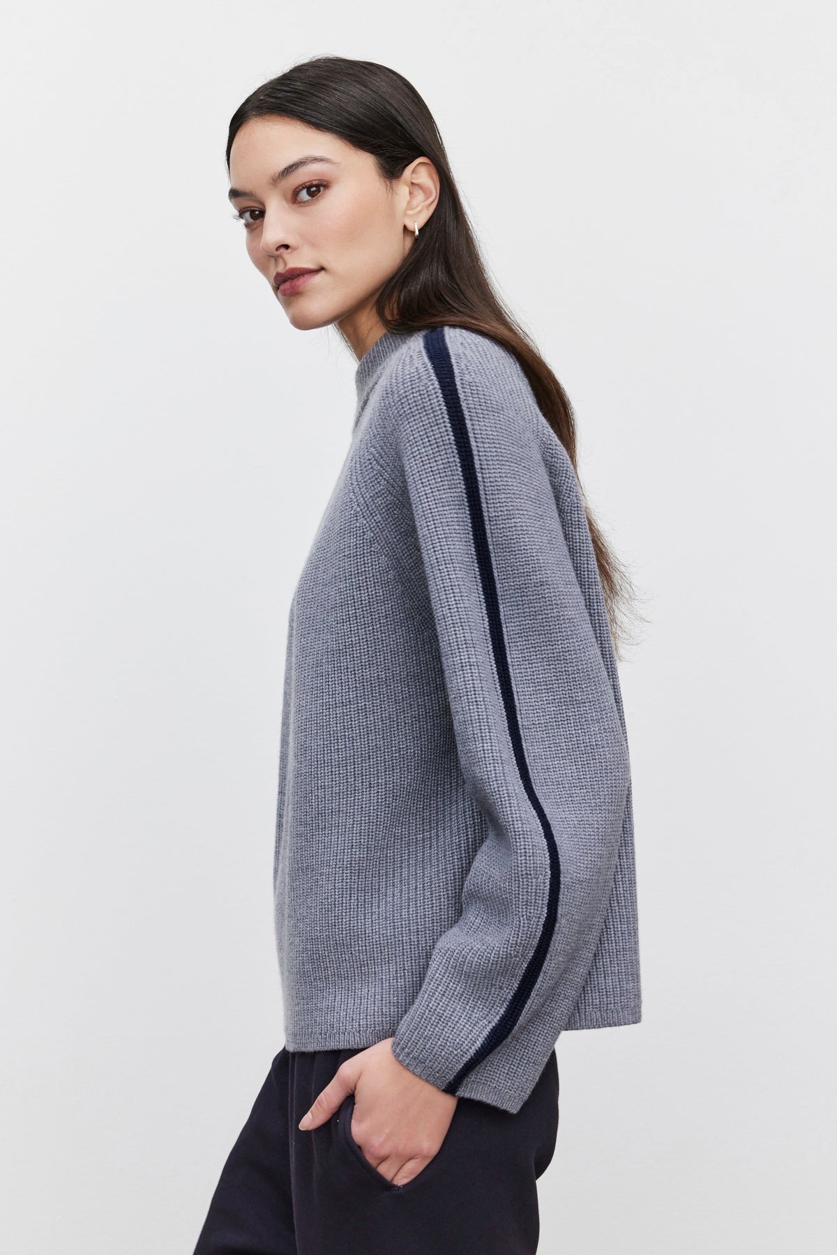   A woman with long dark hair wears the cozy TEAGAN SWEATER by Velvet by Graham & Spencer, which features a dark stripe on the sleeve. She stands against a plain white background. 