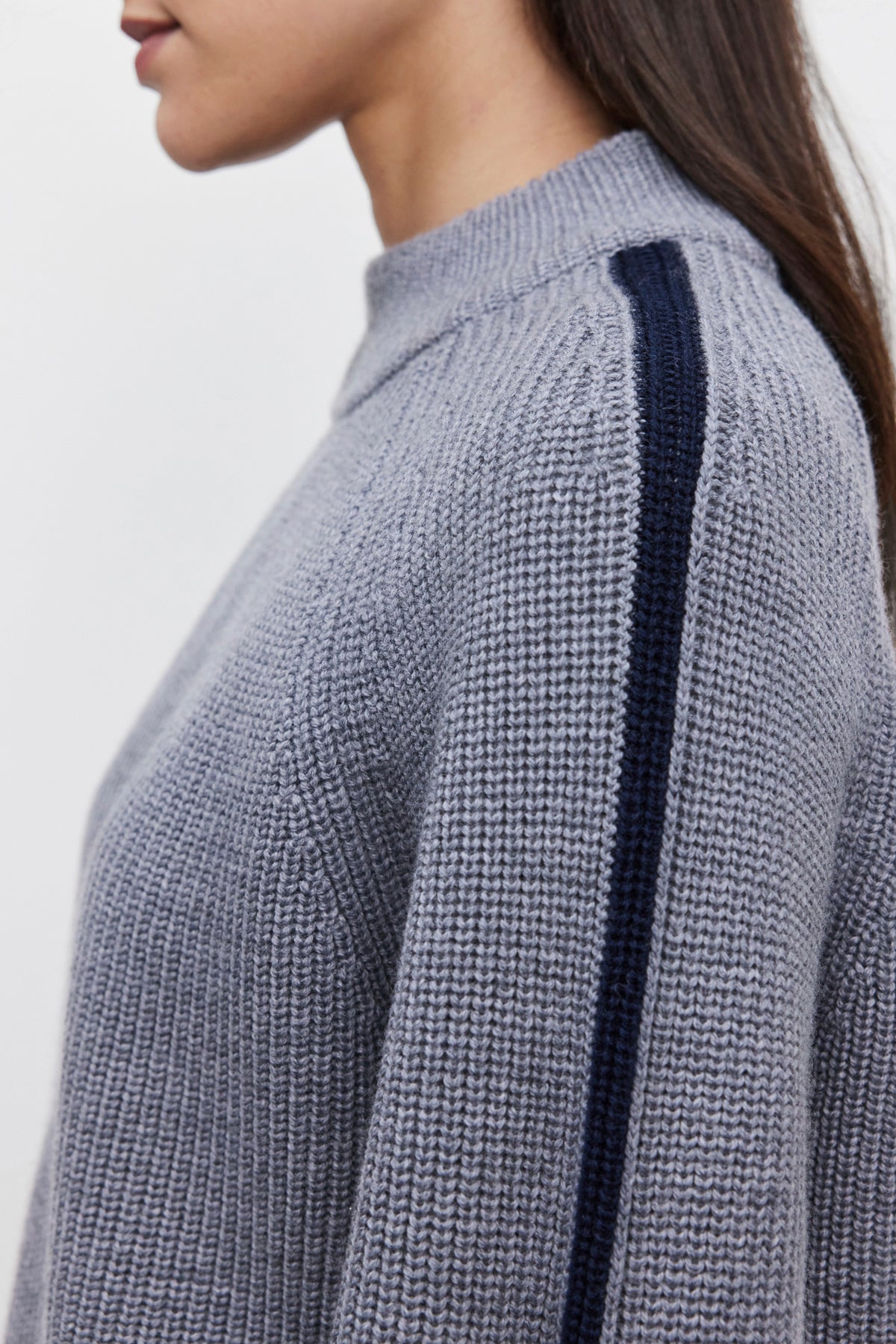   A person wearing the cozy and comfortable TEAGAN SWEATER by Velvet by Graham & Spencer, featuring a blue stripe on the sleeve, viewed from the side. 