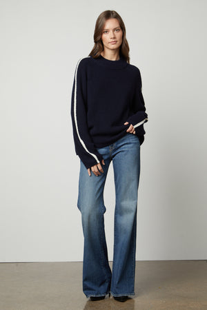 The model is wearing a TEAGAN MOCK NECK SWEATER by Velvet by Graham & Spencer and flared jeans.