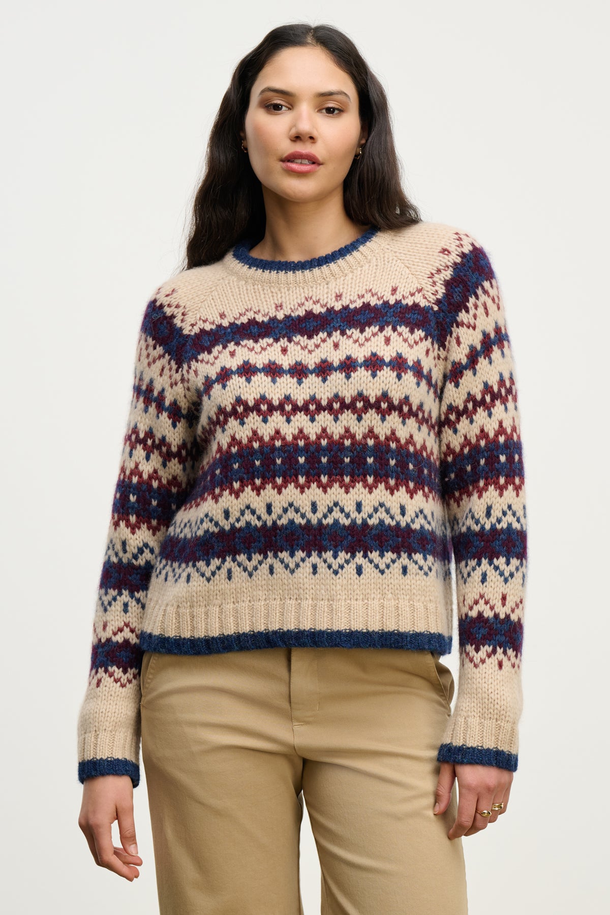 A woman faces forward in the MAKENA ALPACA SWEATER by Velvet by Graham & Spencer, featuring red and blue geometric patterns, styled with khaki pants against a plain background.-39814907658433