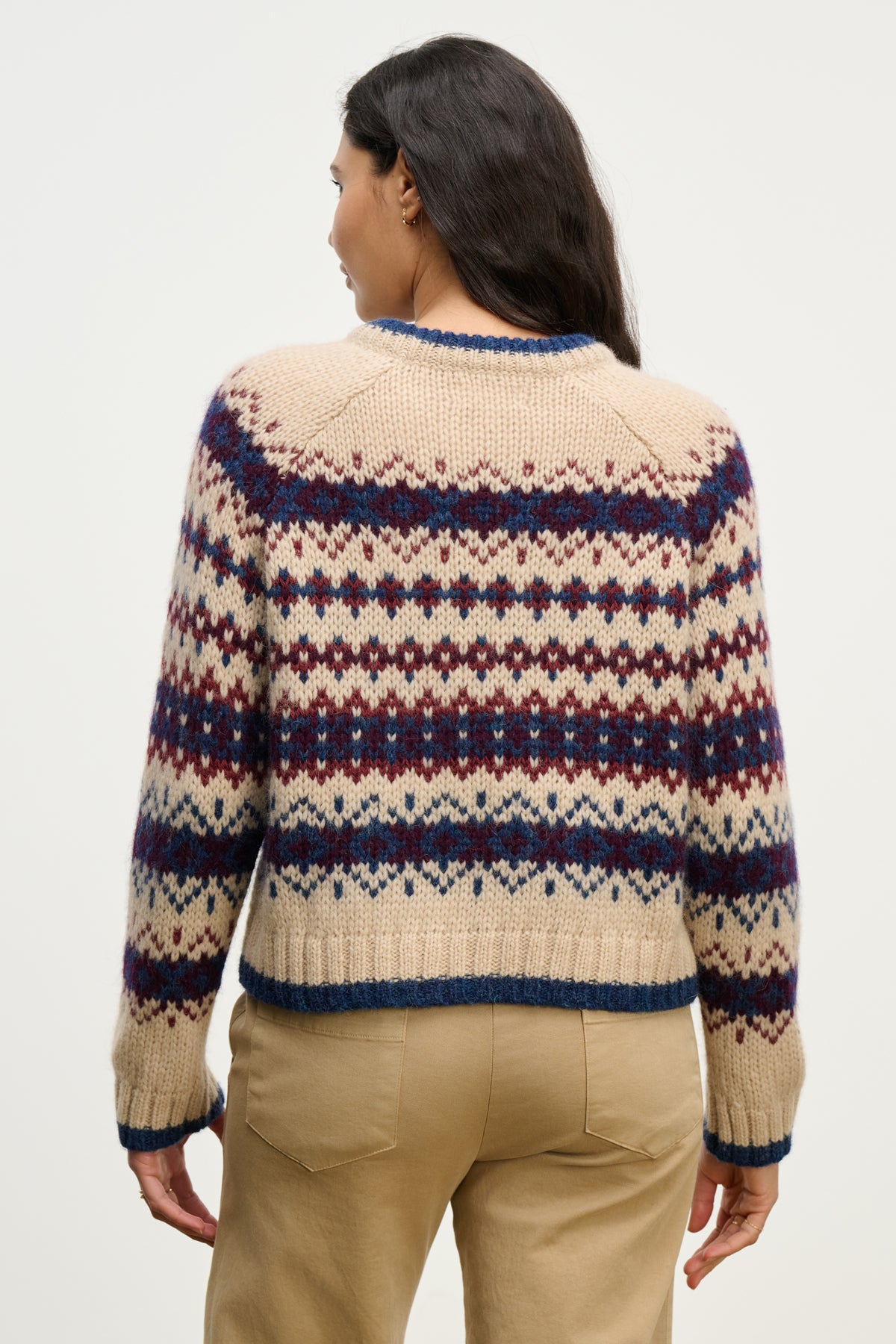A person faces away, wearing the MAKENA ALPACA SWEATER by Velvet by Graham & Spencer—an alpaca blend featuring a blue and burgundy geometric pattern—with tan pants against a plain background.-39814907625665