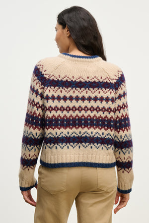 A person faces away, wearing the MAKENA ALPACA SWEATER by Velvet by Graham & Spencer—an alpaca blend featuring a blue and burgundy geometric pattern—with tan pants against a plain background.