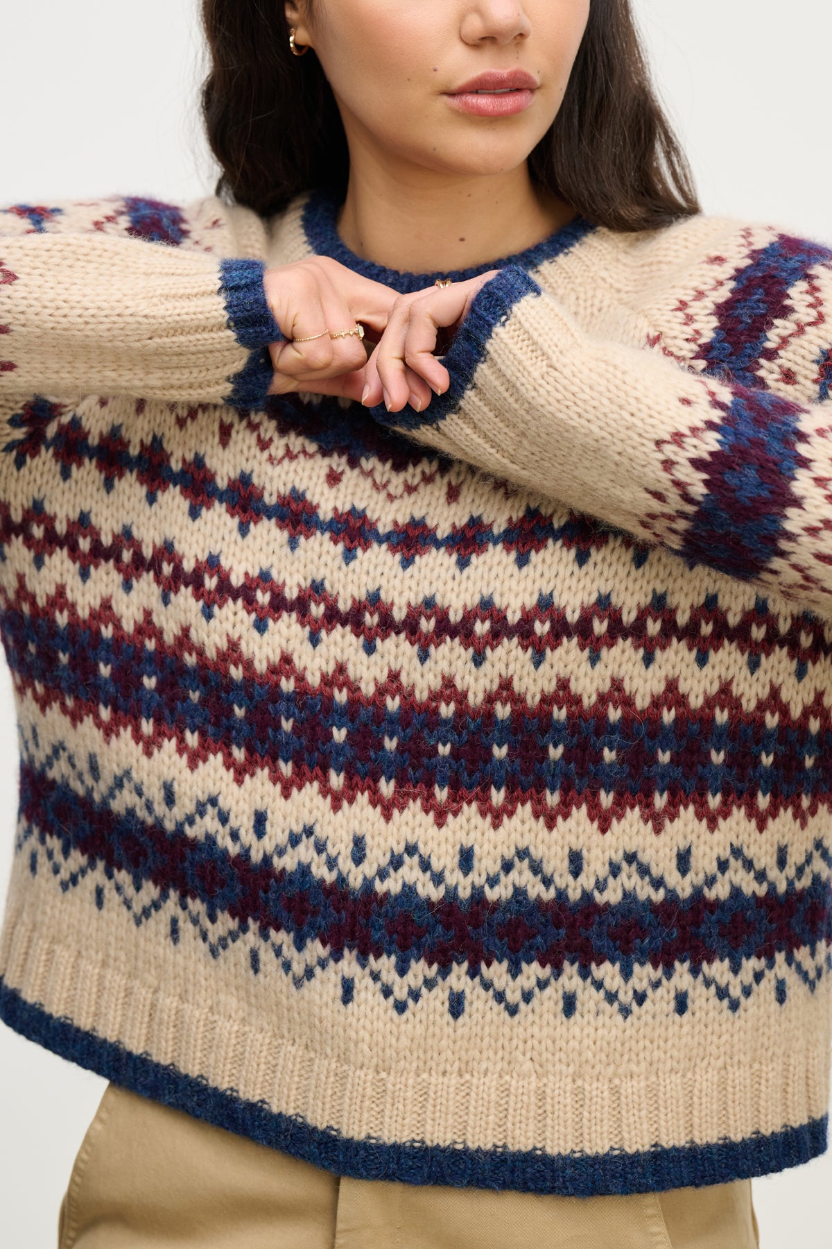 A person in the MAKENA ALPACA SWEATER by Velvet by Graham & Spencer—beige and blue Fair Isle with maroon accents—raises one arm across their chest; their head is partially out of frame.-39814907592897