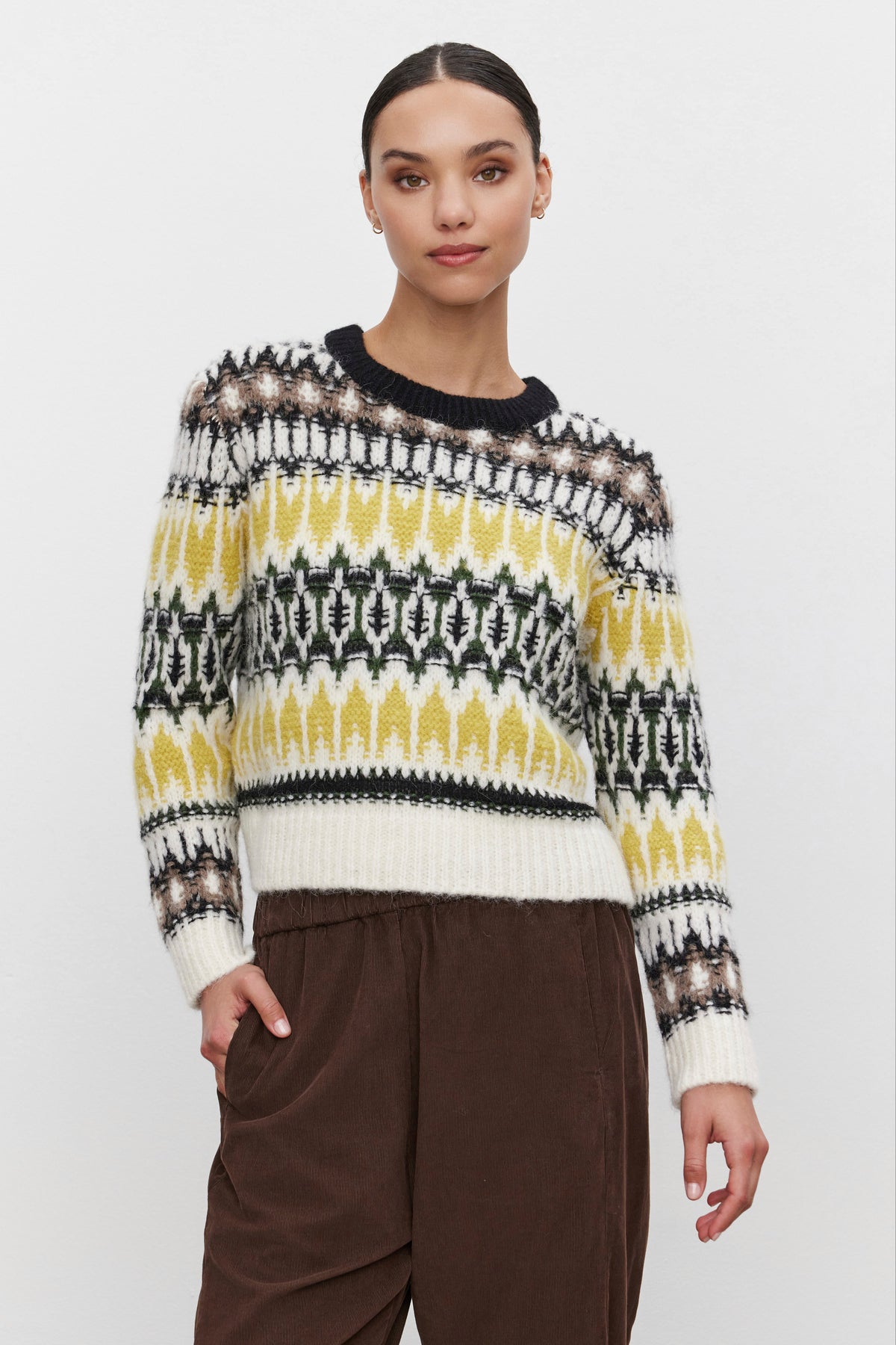 A person dressed in the THELMA ALPACA FAIR ISLE SWEATER by Velvet by Graham & Spencer, featuring yellow, black, and white designs, stands against a plain background.-38373287264449