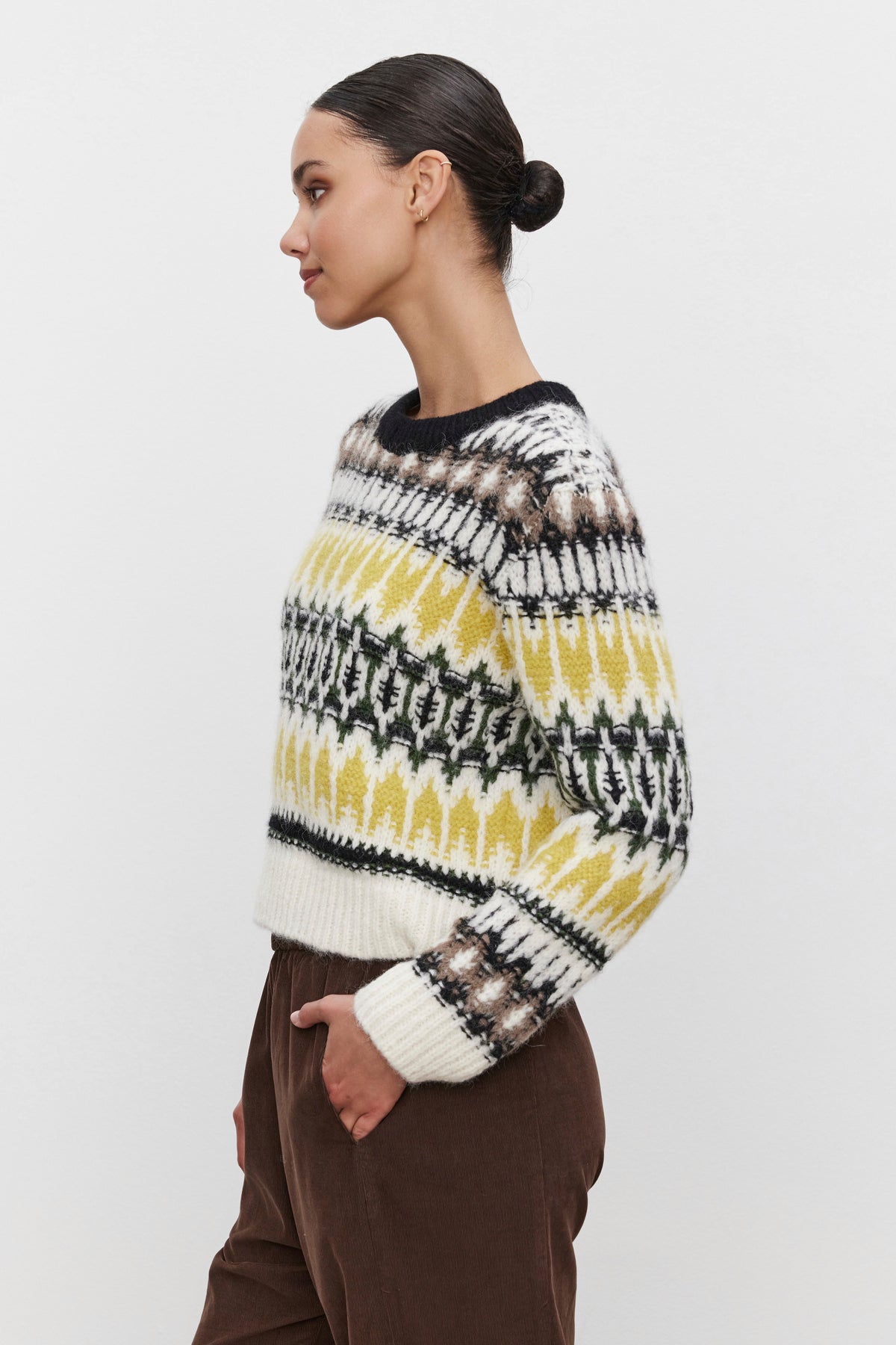 Side profile of a person wearing the THELMA ALPACA FAIR ISLE SWEATER by Velvet by Graham & Spencer, featuring yellow, black, and white designs, paired with brown pants against a white background.-38373287297217