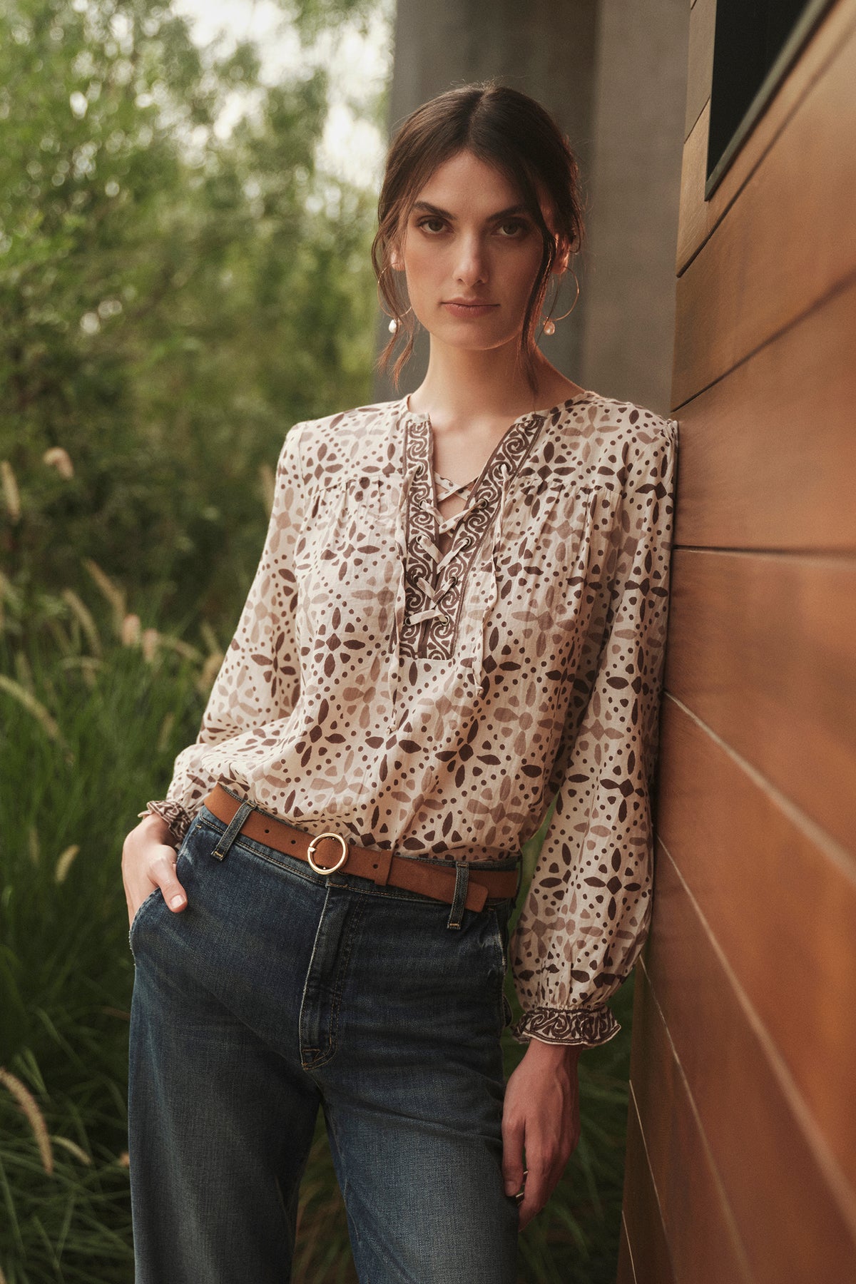A woman wearing jeans and a AUDETTE PRINTED BOHO TOP by Velvet by Graham & Spencer leaning against a wall.-26887731970241