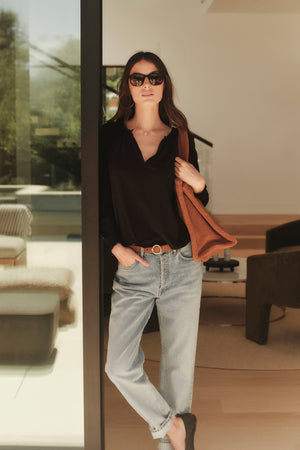 A woman in a black Velvet by Graham & Spencer top and jeans standing in front of a glass door.