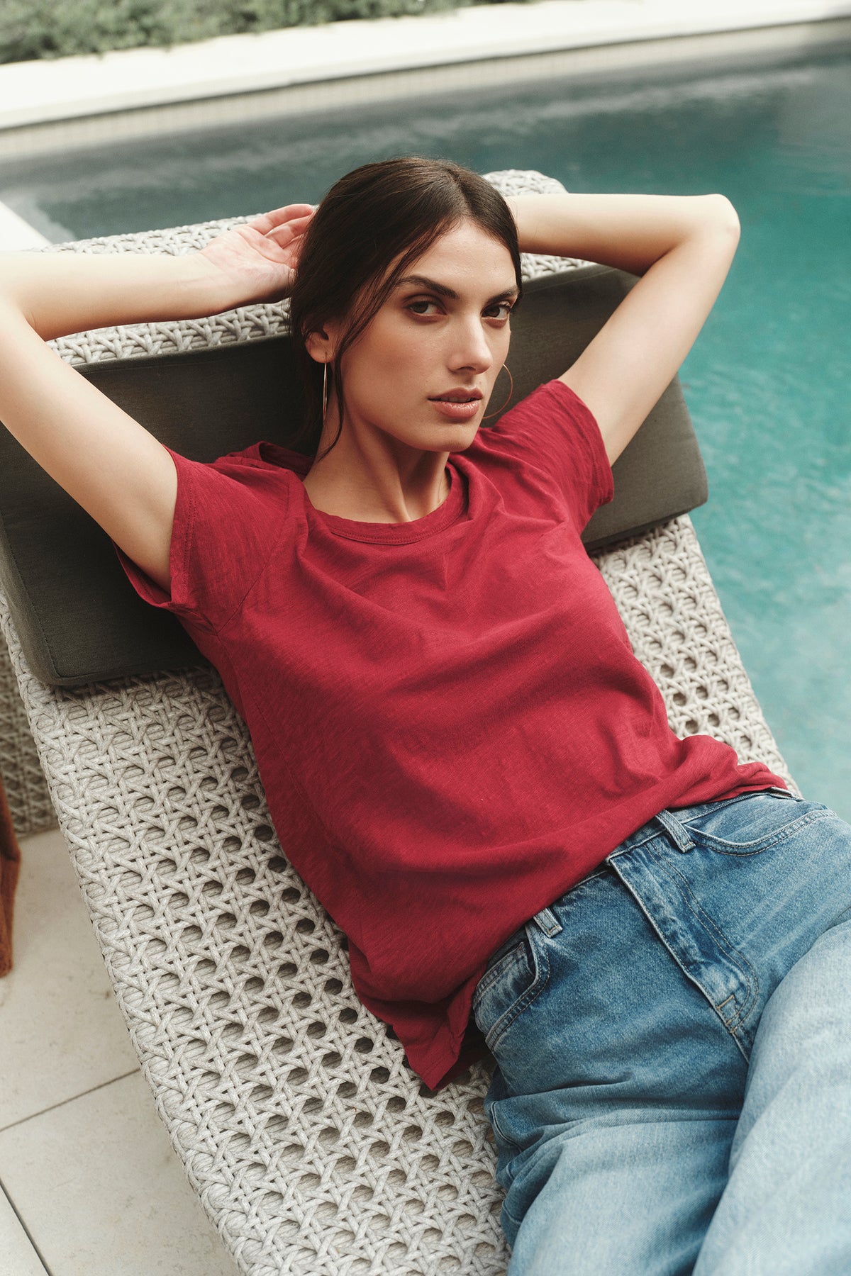   A woman in a red Velvet by Graham & Spencer TILLY ORIGINAL SLUB CREW NECK TEE is laying on a lounge chair in front of a pool. 