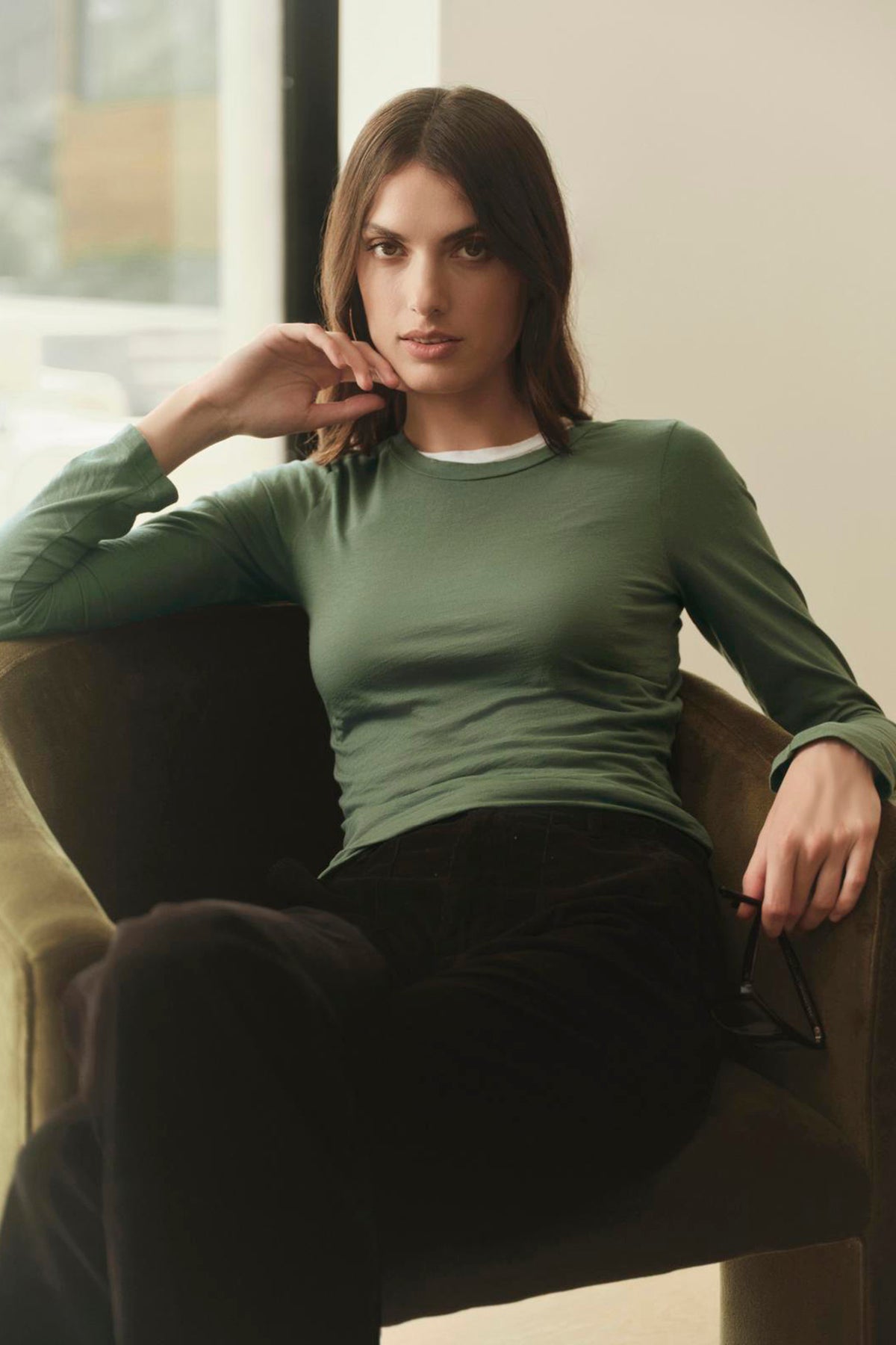 A woman sitting on a chair in a Velvet by Graham & Spencer ZOFINA GAUZY WHISPER FITTED CREW NECK TEE.-35783262470337