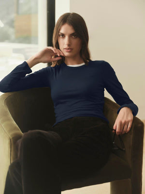 A woman wearing Velvet by Graham & Spencer's ZOFINA GAUZY WHISPER FITTED CREW NECK TEE, a navy long-sleeved shirt, sitting in a chair.
