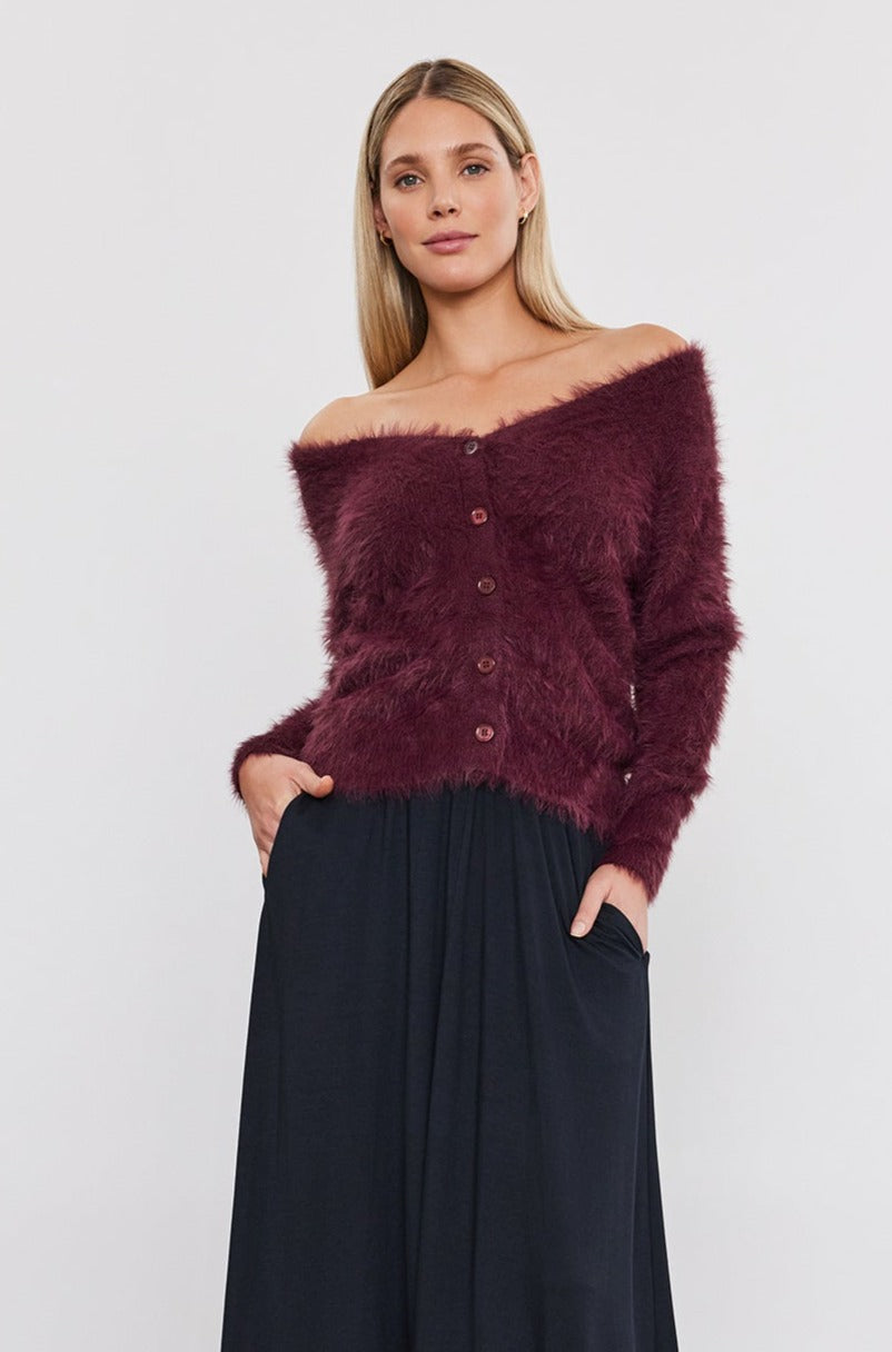 The model is wearing a burgundy Velvet by Graham & Spencer soft ELLE FEATHER YARN CARDIGAN knit sweater, paired with a black pleated skirt.