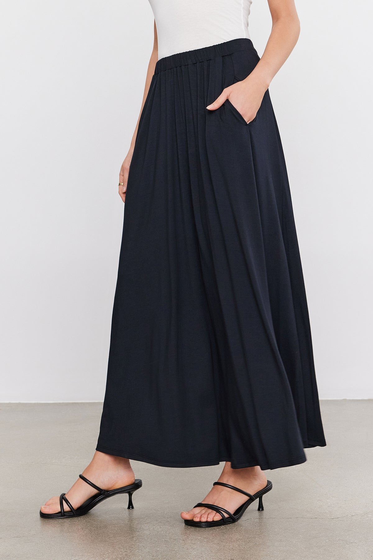   A woman wearing a navy pleated MALAYA MAXI SKIRT by Velvet by Graham & Spencer. 