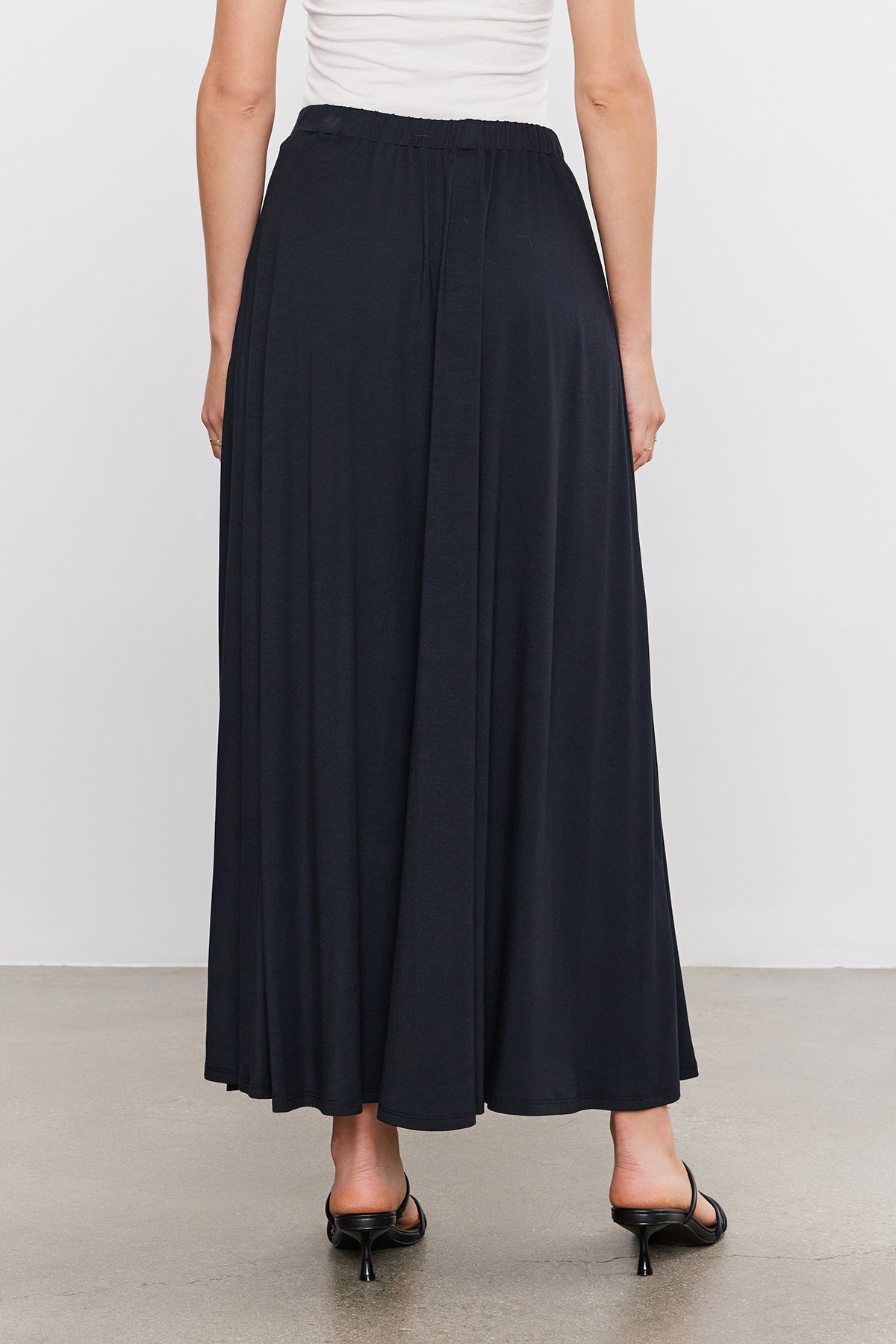   The back view of a woman wearing a Velvet by Graham & Spencer Malaya Maxi Skirt in an A-line silhouette. 