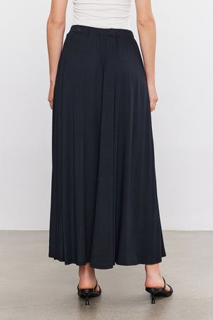 The back view of a woman wearing a Velvet by Graham & Spencer Malaya Maxi Skirt in an A-line silhouette.