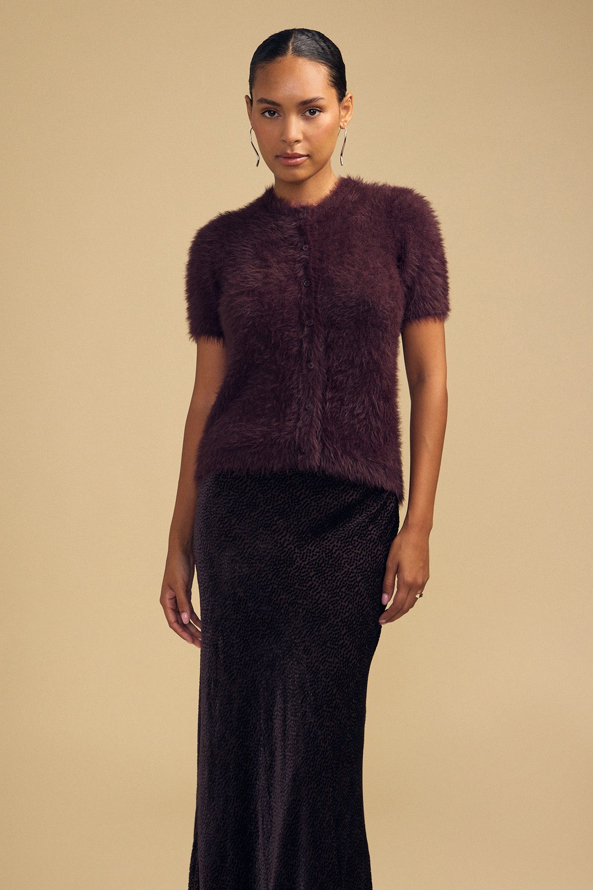 A woman wearing a soft, airy, short-sleeved dark purple GABBY FEATHER YARN CARDIGAN by Velvet by Graham & Spencer and a dark patterned midi skirt.