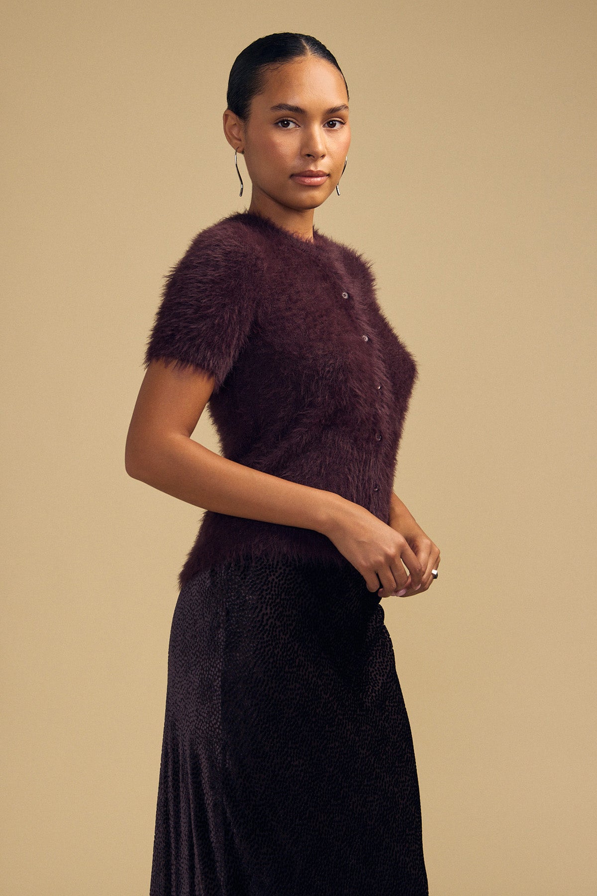 A person wearing a short-sleeved, dark burgundy GABBY FEATHER YARN CARDIGAN by Velvet by Graham & Spencer, featuring a soft, airy, textured knit.