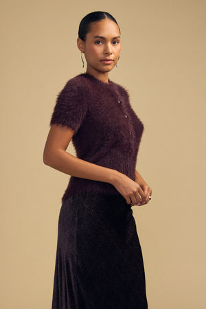 A person wearing a short-sleeved, dark burgundy GABBY FEATHER YARN CARDIGAN by Velvet by Graham & Spencer, featuring a soft, airy, textured knit.