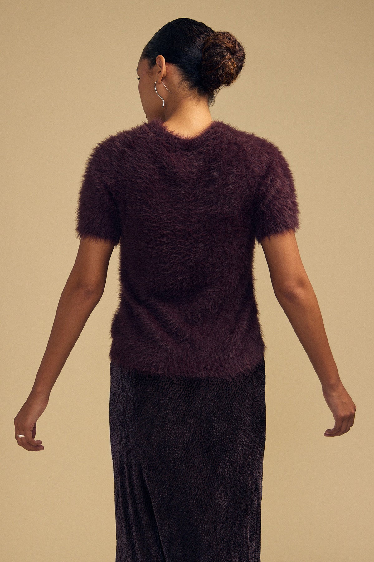A dark purple, short-sleeved GABBY FEATHER YARN CARDIGAN in fuzzy, lightweight yarn, worn with a dark skirt and viewed from behind.