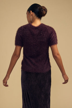 A dark purple, short-sleeved GABBY FEATHER YARN CARDIGAN in fuzzy, lightweight yarn, worn with a dark skirt and viewed from behind.