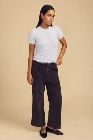 A person wears a soft, light blue GABBY FEATHER YARN CARDIGAN with dark brown wide-leg pants and black Mary Jane flats.