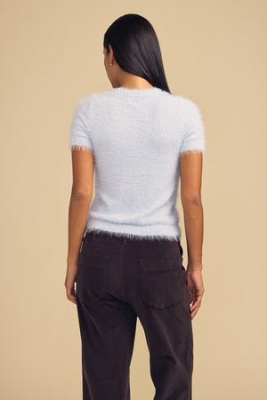 Back view of a person wearing a light blue GABBY FEATHER YARN CARDIGAN and dark pants.