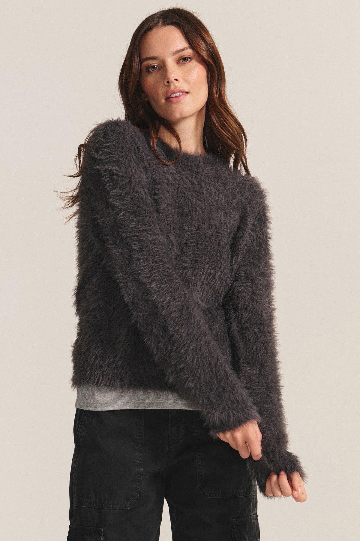 A woman in the PENNY SWEATER by Velvet by Graham & Spencer—a long-sleeve, dark gray fuzzy top made from lightweight feather yarn—and black pants stands against a plain light background.-40248224350401