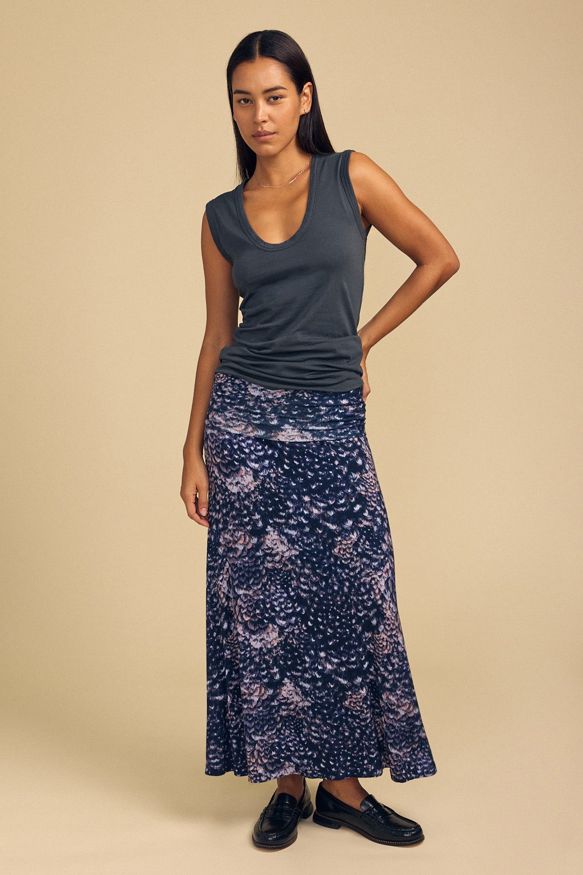 A woman wears a sleeveless dark gray tank top and a dark blue VALERIE PRINTED SKIRT paired with black loafers.