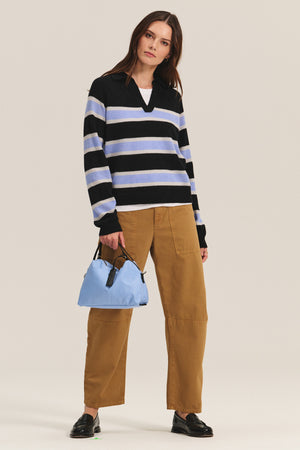 A woman stands against a plain background wearing the EVERLAKE SWEATER POLO by Velvet by Graham & Spencer, paired with tan wide-leg pants, black loafers, and holding a light blue handbag.