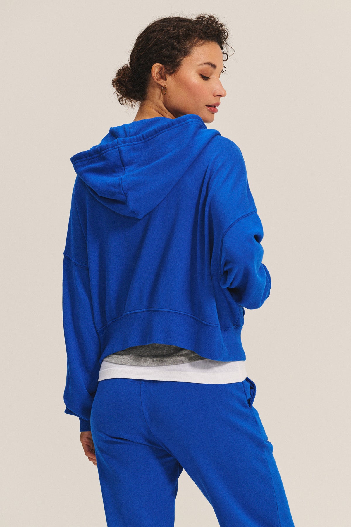 A person with short curly hair is seen from the back wearing Velvet by Graham & Spencer’s royal blue HIGHLAND HOODIE and matching pants—ideal comfy loungewear against a neutral background.-40672298401985