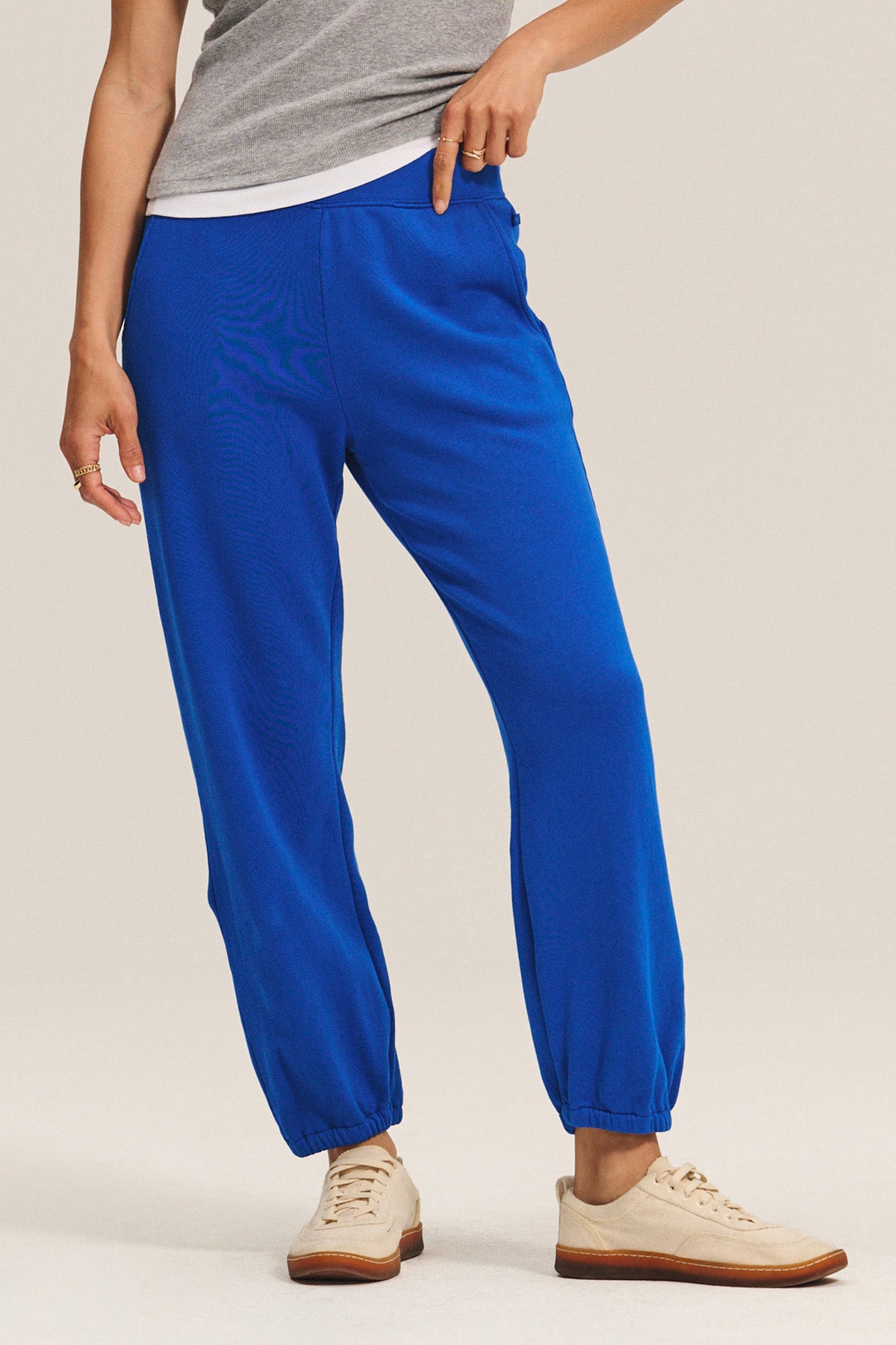 A person wearing relaxed fit bright blue ZARA SWEATPANT jogger pants by Velvet by Graham & Spencer, a grey top, and beige sneakers stands against a neutral background.-40672511131841