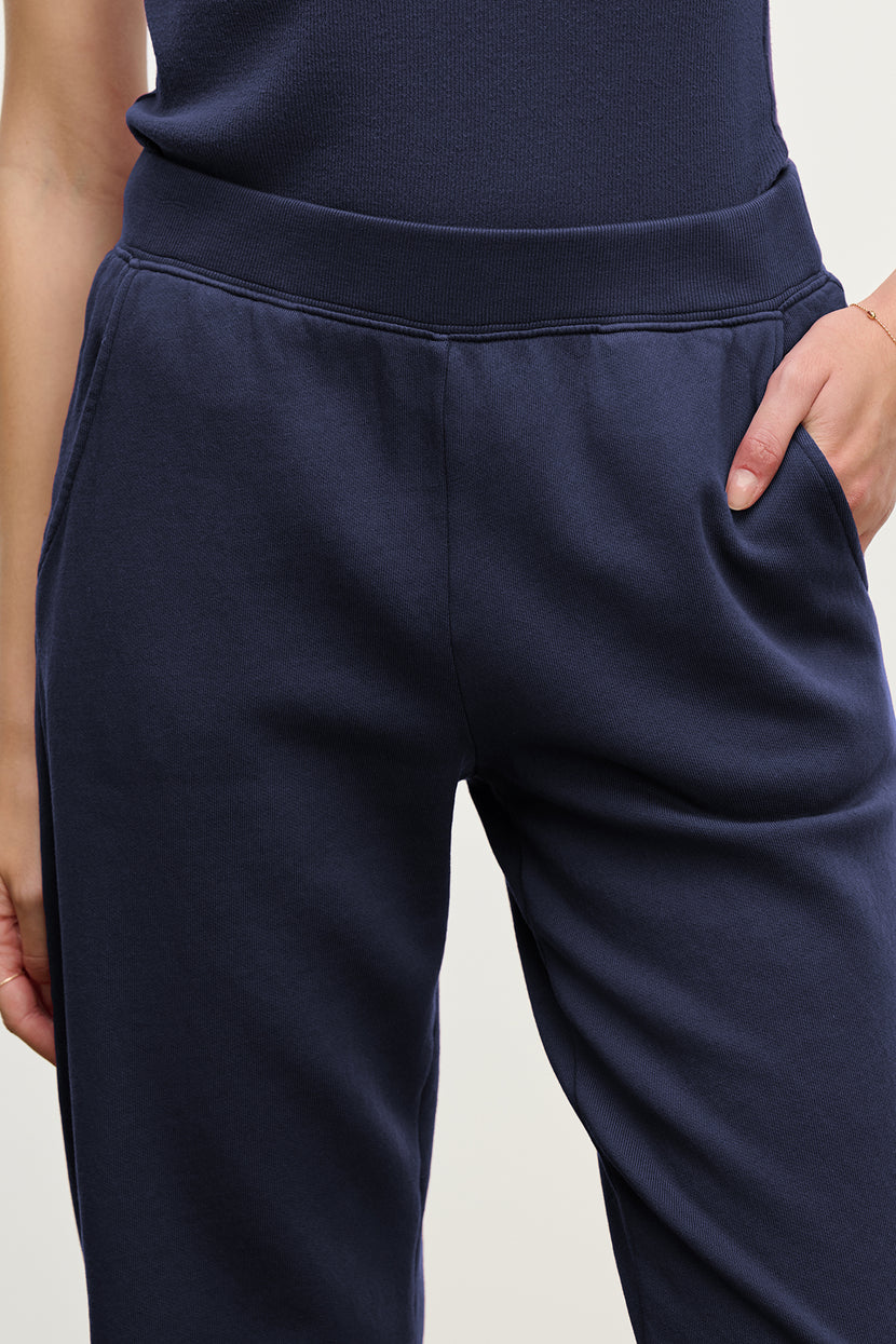 Model wearing Velvet by Jenny Graham's ZUMA SWEATPANT in navy organic cotton, hand in pocket, shown waist to mid-thigh.