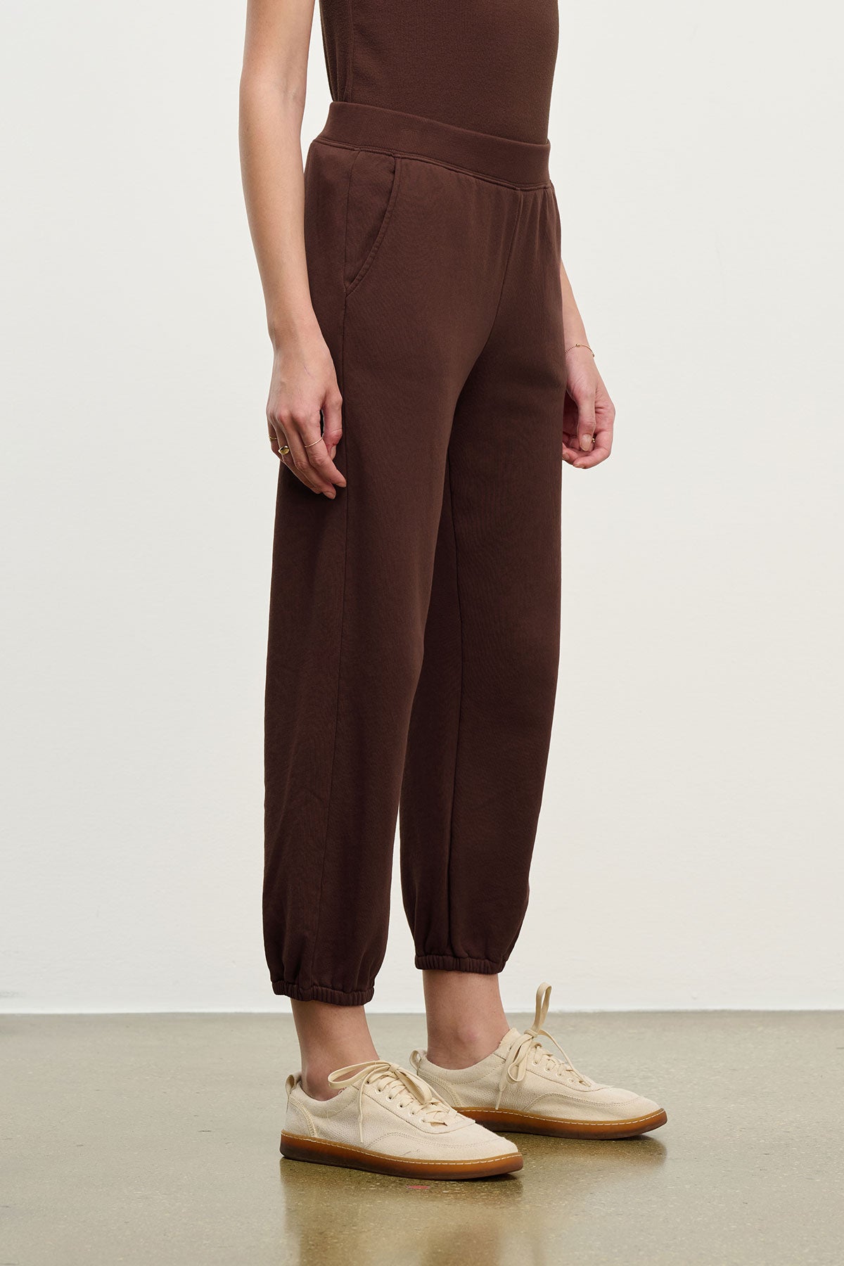 A person wears relaxed fit brown ZARA SWEATPANT from Velvet by Graham & Spencer in soft cotton fleece with beige sneakers, standing against a plain background and facing slightly to the side.