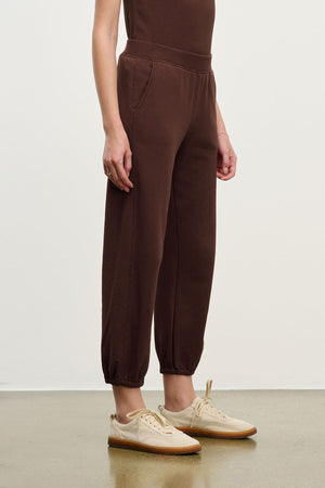 A person wears relaxed fit brown ZARA SWEATPANT from Velvet by Graham & Spencer in soft cotton fleece with beige sneakers, standing against a plain background and facing slightly to the side.