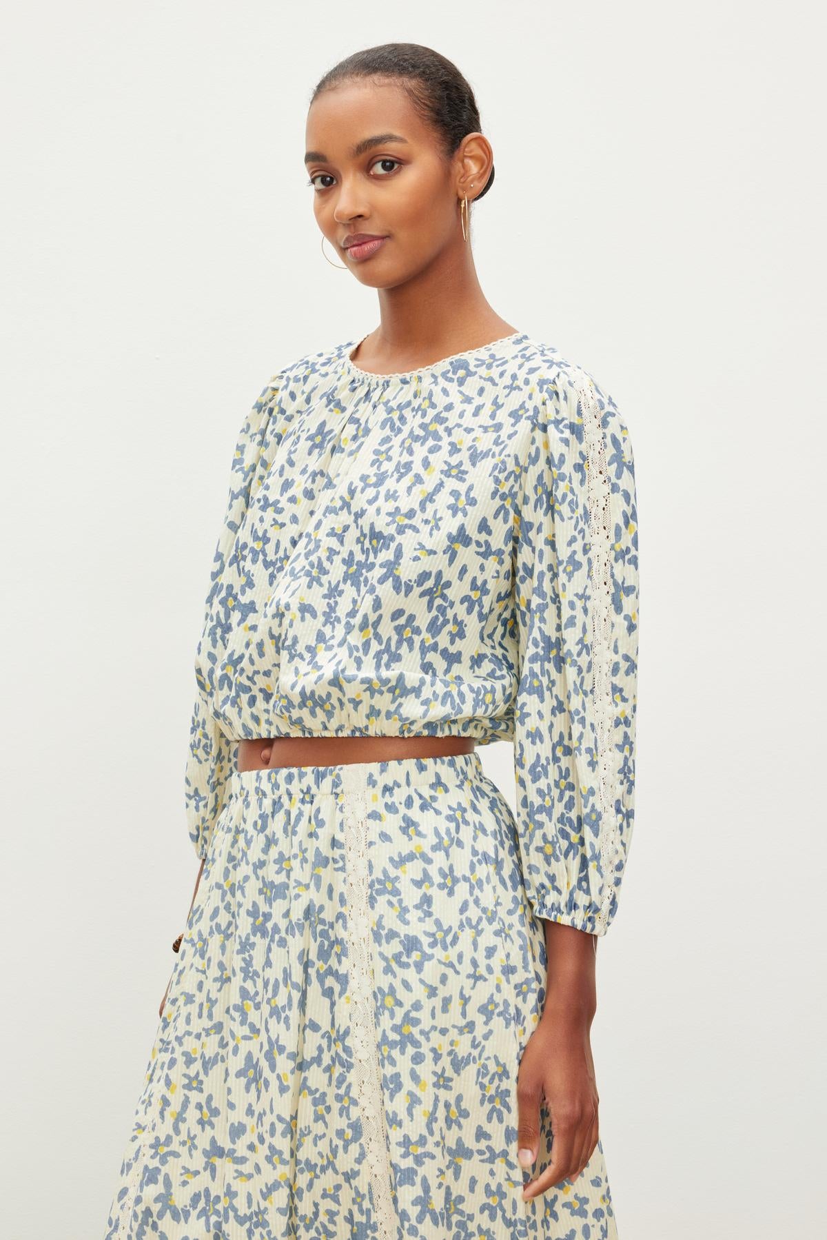   A person wearing a matching long-sleeved CAMERON TOP and skirt with a blue and yellow leaf pattern, standing against a plain white background, by Velvet by Graham & Spencer. 