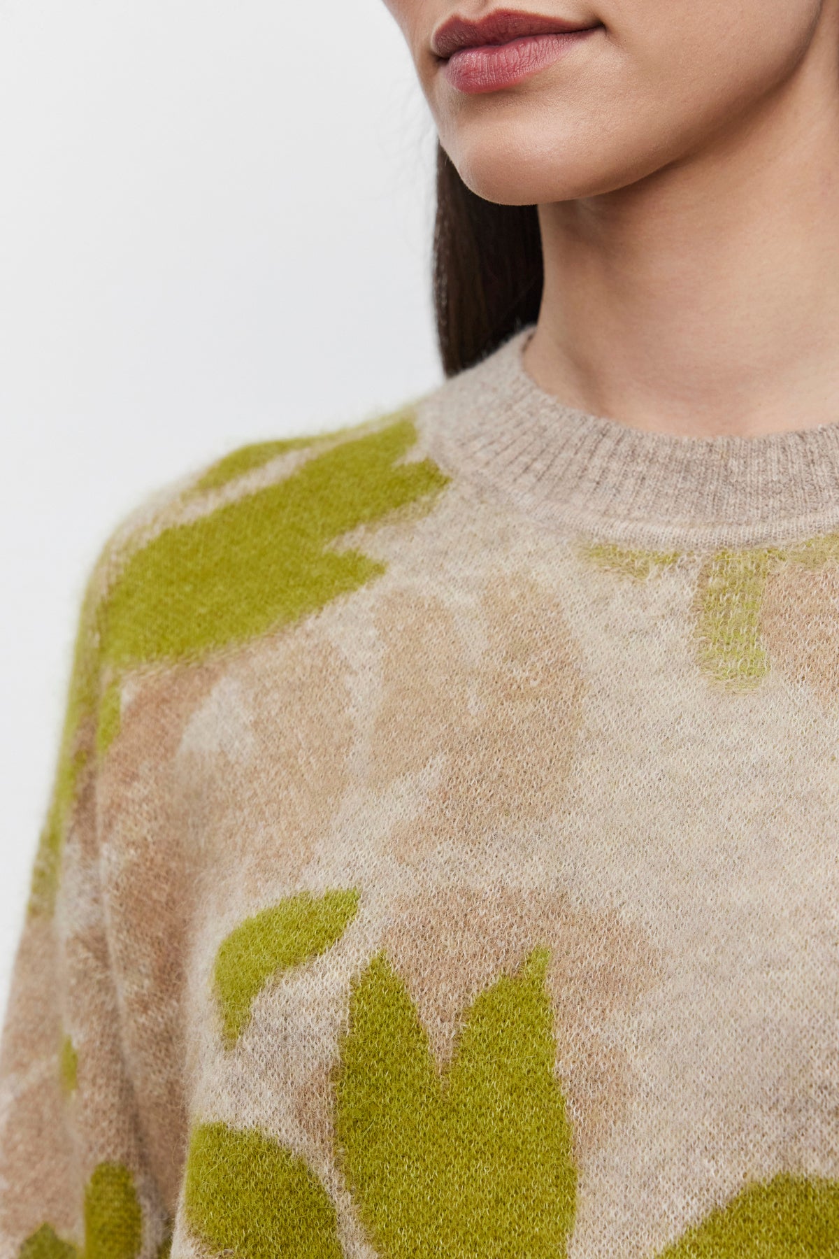   Close-up of a person's upper torso, showcasing the RIVA SWEATER by Velvet by Graham & Spencer, featuring a beige and green floral jacquard pattern made from a soft alpaca blend, and part of their face. 