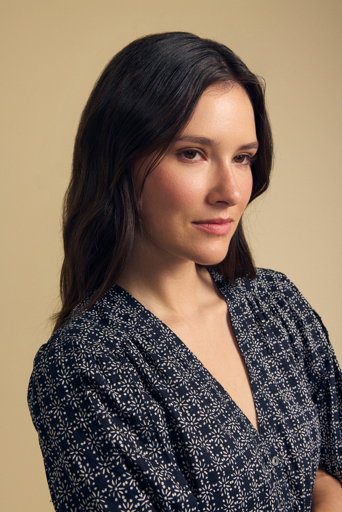 A woman with long brown hair wears the IMANI BLOUSE by Velvet by Graham & Spencer and looks to the side against a plain beige background.-41826786443457