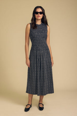 A woman stands against a plain background wearing the KATHERINE DRESS by Velvet by Graham & Spencer—a sleeveless floral midi dress perfect for summer—paired with black sunglasses and black shoes.