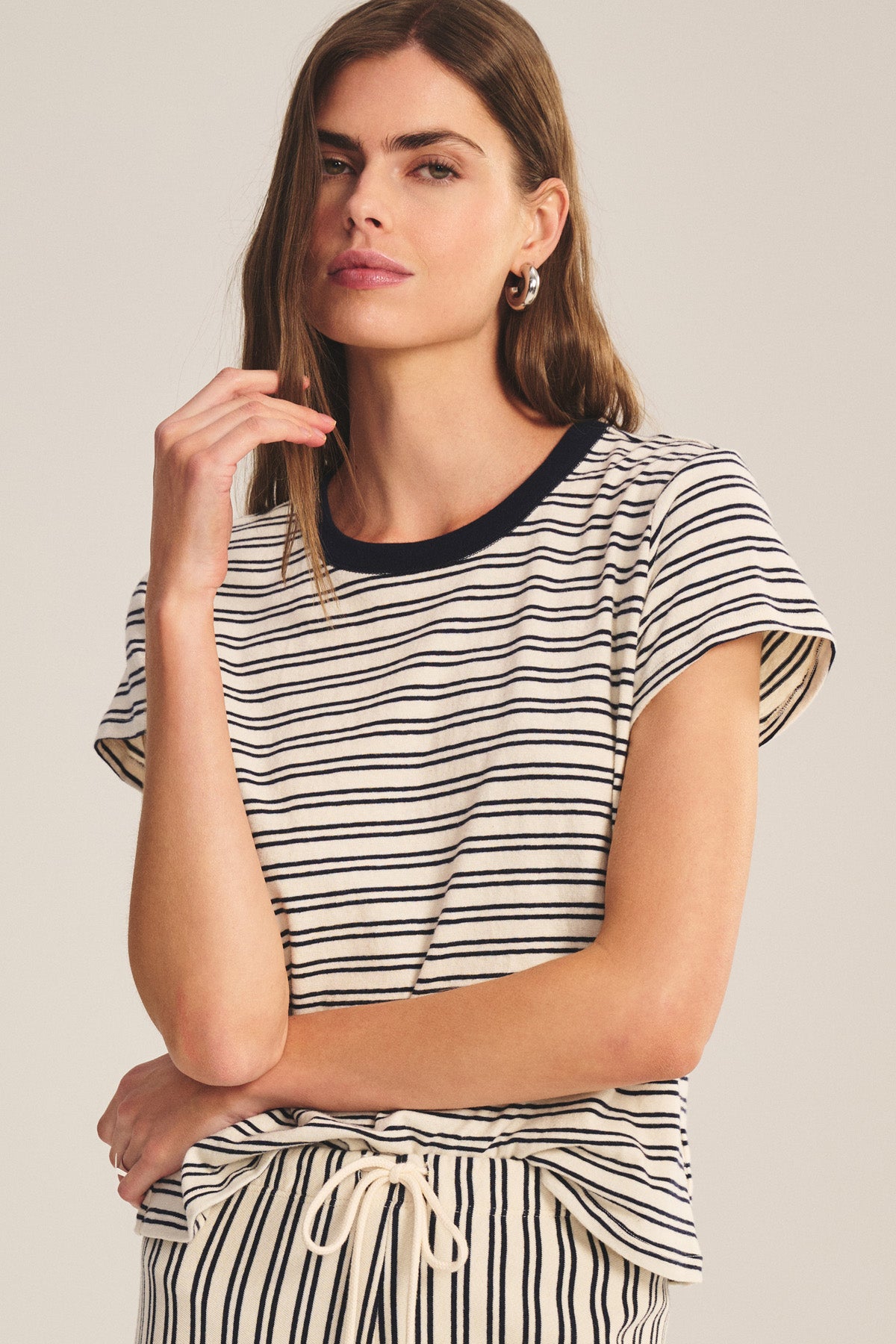 A woman wears the Velvet by Graham & Spencer FOSTER TEE—a short-sleeve, black and white striped jersey cropped top—paired with matching striped pants, standing against a neutral background.-40909835141313