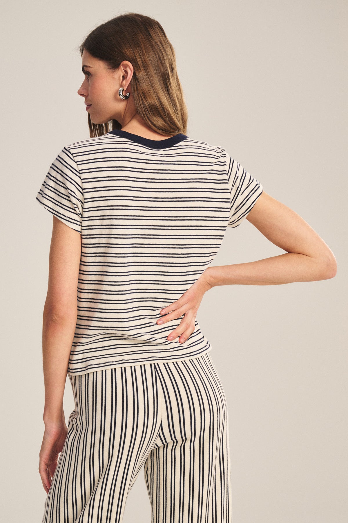 A woman faces away from the camera wearing the Velvet by Graham & Spencer FOSTER TEE, a cream and black striped cropped jersey top with matching pants and a contrast crew neckline.