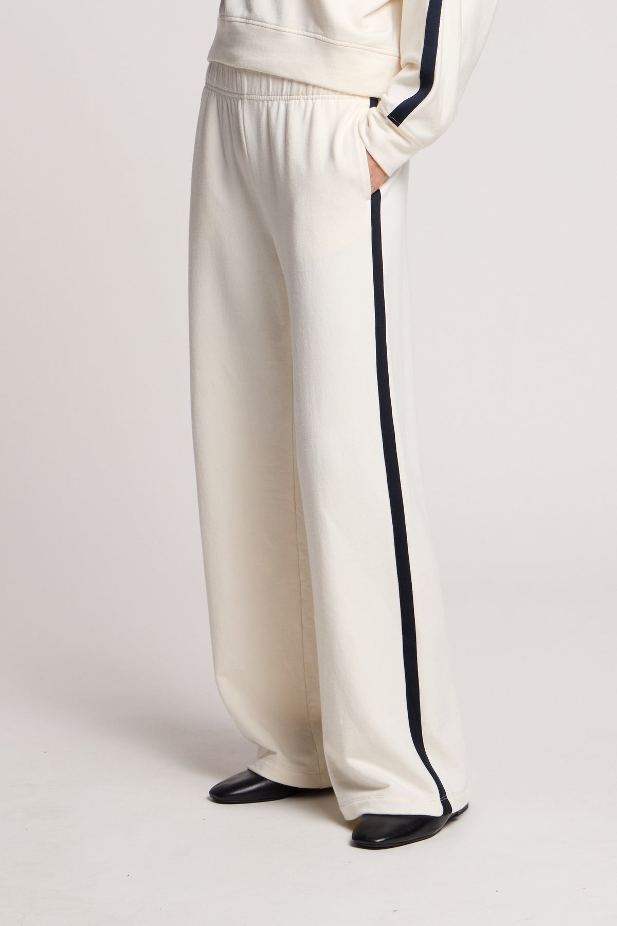 Model wears the GIGI SWEATPANT by Velvet by Graham & Spencer, featuring a relaxed fit, cream color, wide legs, and black side stripes with black shoes against a plain background.-40732642640065