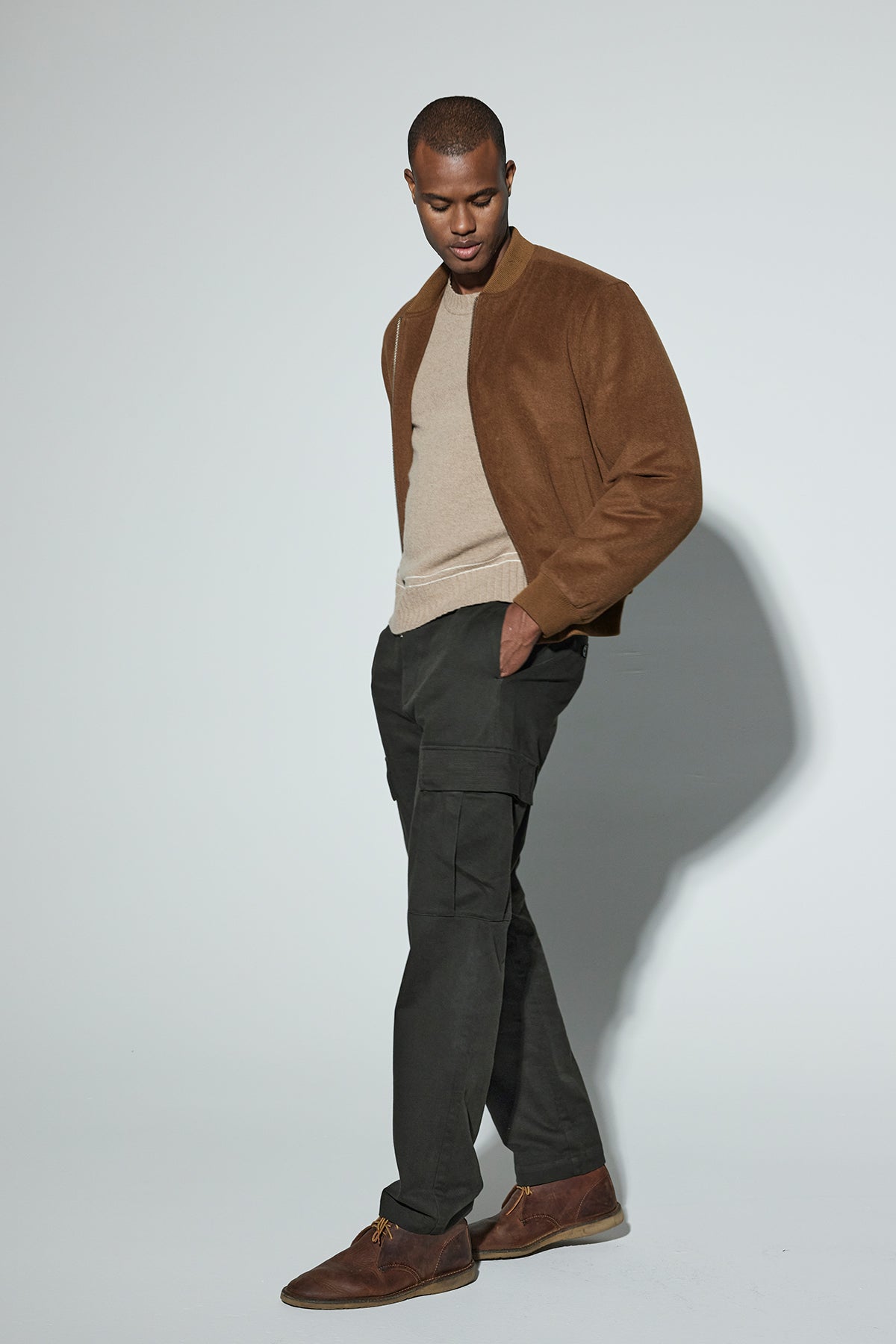   A person wearing a brown jacket over the ATTICUS SWEATER with contrast stripe detail by Velvet by Graham & Spencer and dark pants stands against a plain background. 